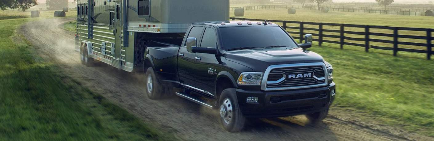 black 2018 Ram 3500 towing a large trailer camper on a dirt road by a farm