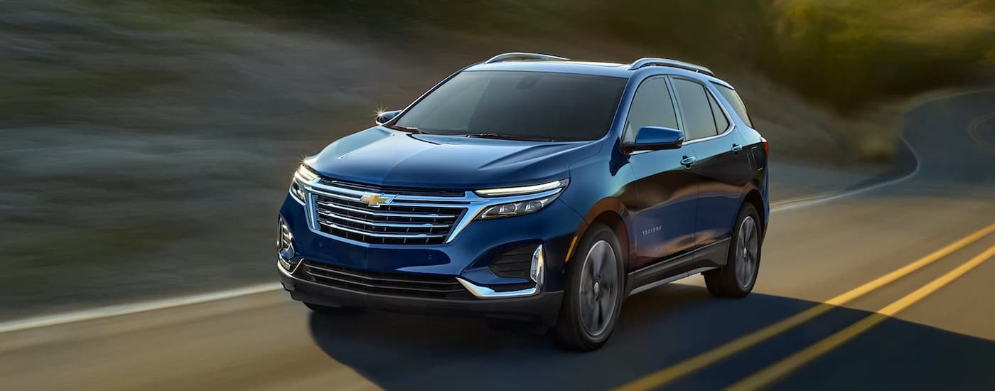 A blue 2022 Chevy Equinox, an SUV for sale near Newark, is driving on a winding road.