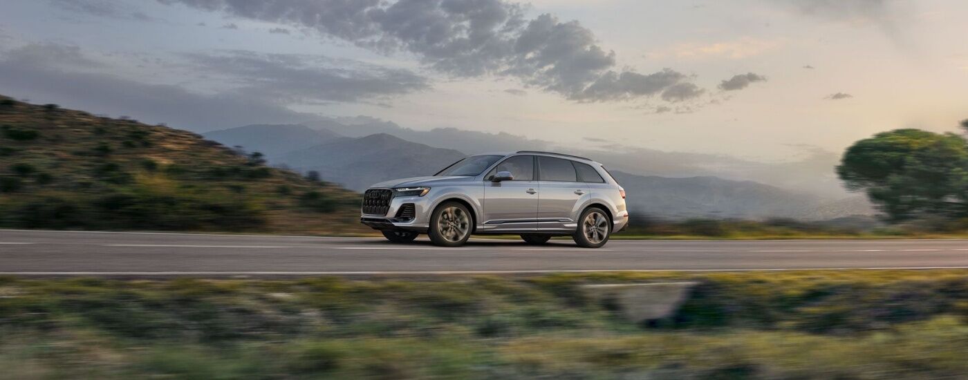 Silver used 2025 Audi Q7 for sale driving on a hilly road