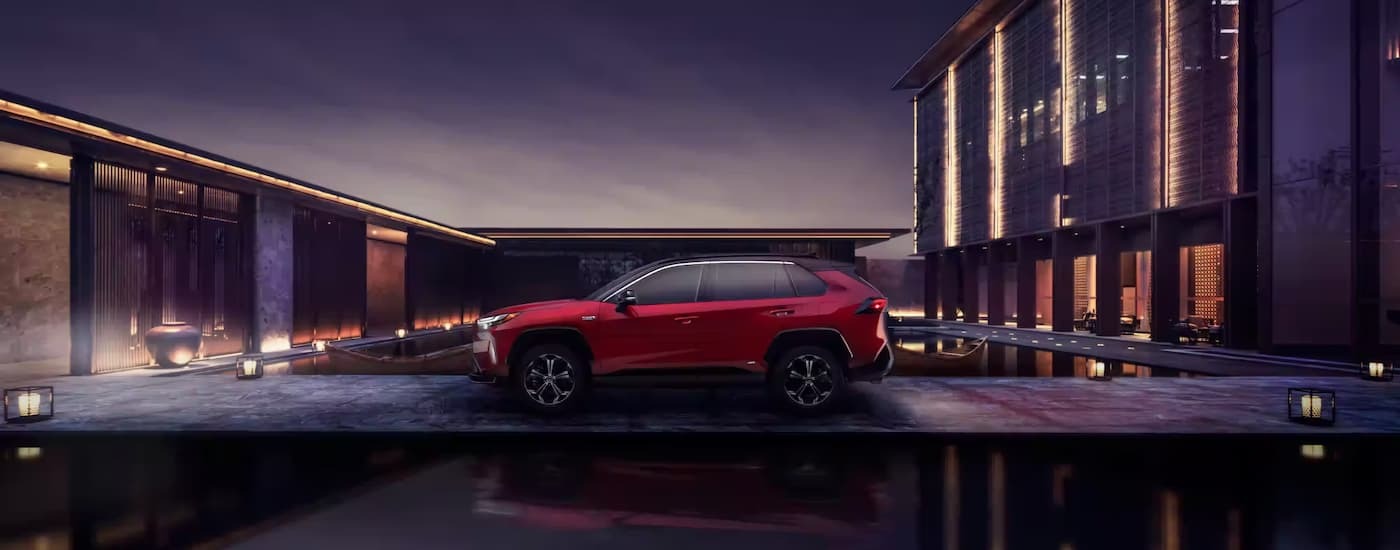 A side view of a red 2023 Toyota RAV4 Prime parked outside of a modern home.