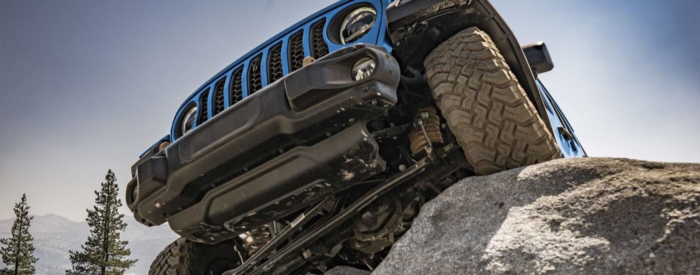 Close up of the front of a blue 2022 Jeep Wrangler off-roading on rocks