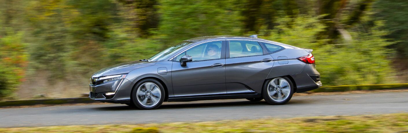 side view of the 2018 Honda Clarity Plug-in Hybrid driving past blurred trees and bushes