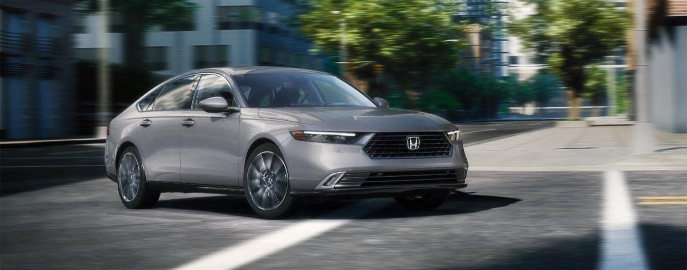 A silver 2024 Honda Accord Touring Hybrid driving in a city