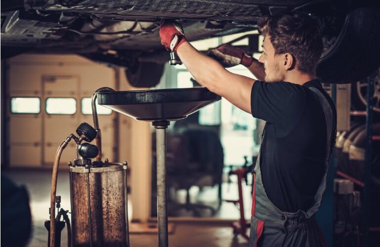 A handsome man is about to drain oil from the bottom of a vehicle into a funnel. A handsome man is about to drain oil from the bottom of a vehicle into a funnel.