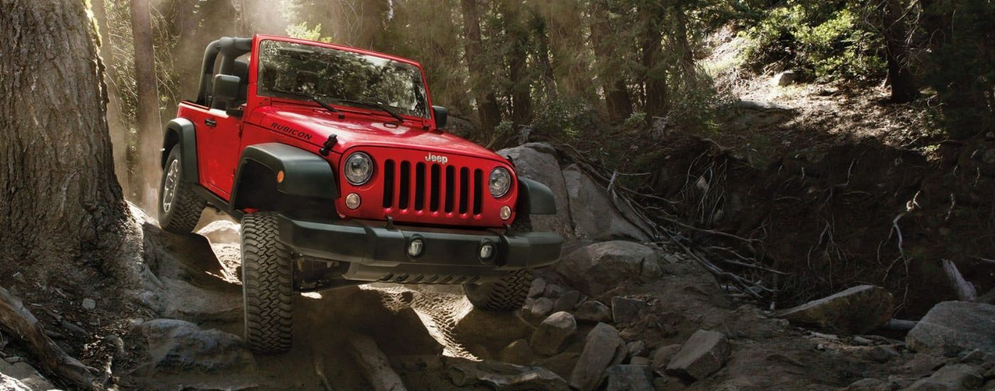 Red 2017 Jeep Wrangler Rubicon driving off-road in a forest.