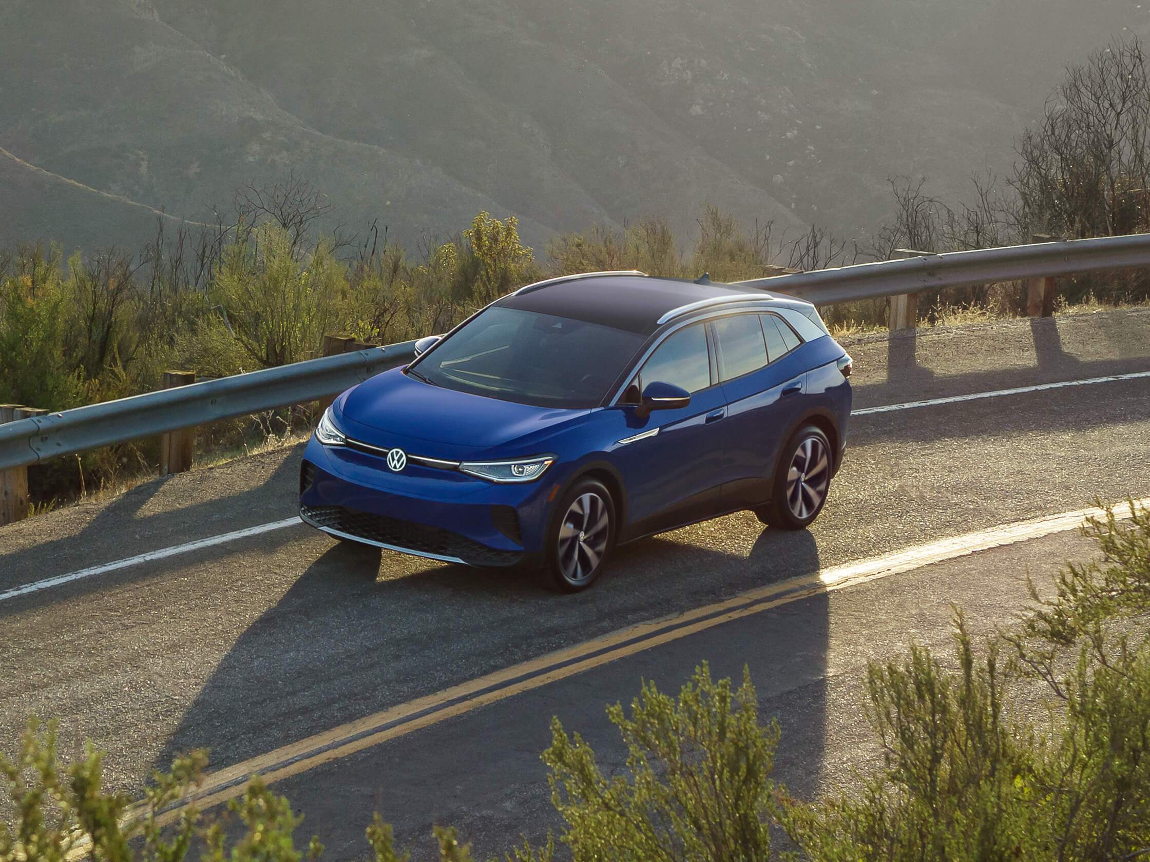 An ID.4 in Dusk Blue Metallic drives along a single-lane highway. An ID.4 in Dusk Blue Metallic drives along a single-lane highway.