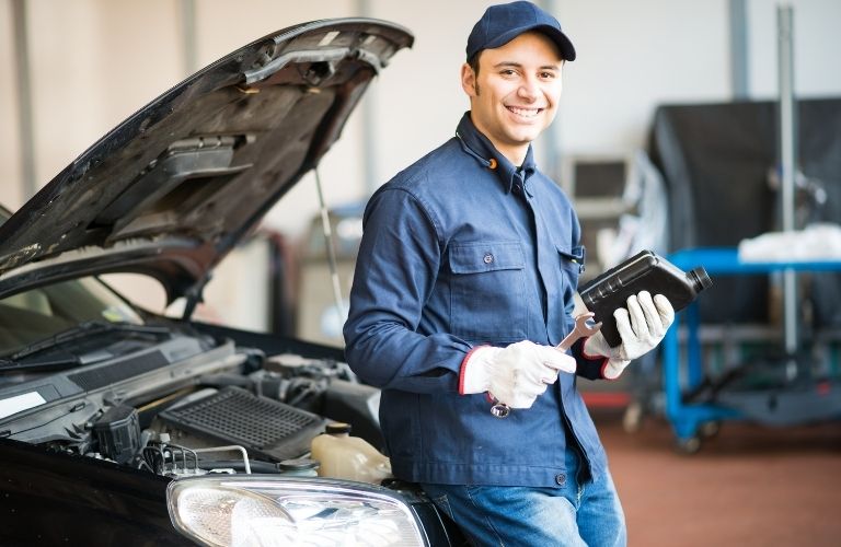 Technician standing against a vehicle with tools and a book in hand