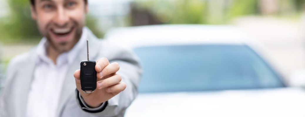 individual showing a key to the camera with a car in the background