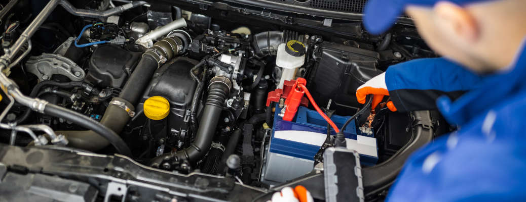 A mechanic is working on a car's battery in a garage