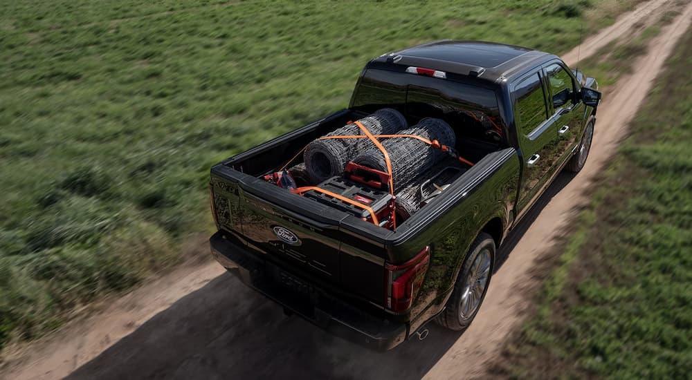 Black used 2024 Ford F-150 for sale driving on a dirt road through a farm