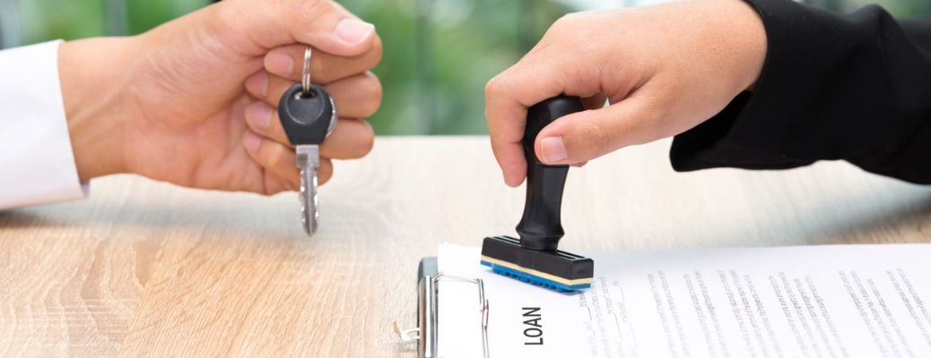 One hand stamping a car loan application and another handing over the keys