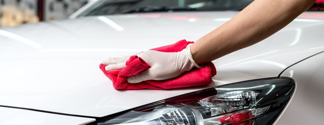 a white-gloved hand cleaning a white car with a red rag