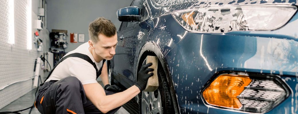 a man washing the wheel and tire of a car