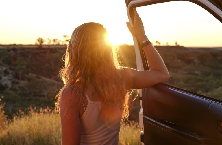 representative image of a woman on a road trip looking at the sunset