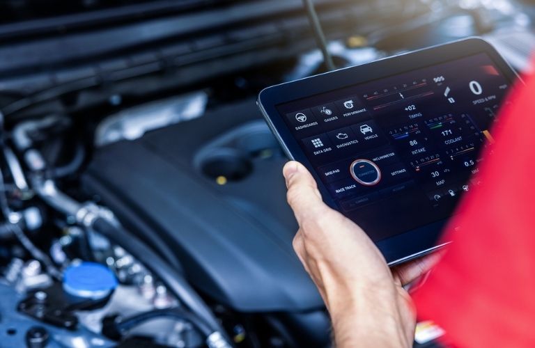 a technician holding a tab in front of an open-hooded car