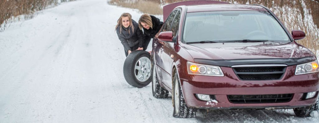 Two women changing a tire on a snowy road