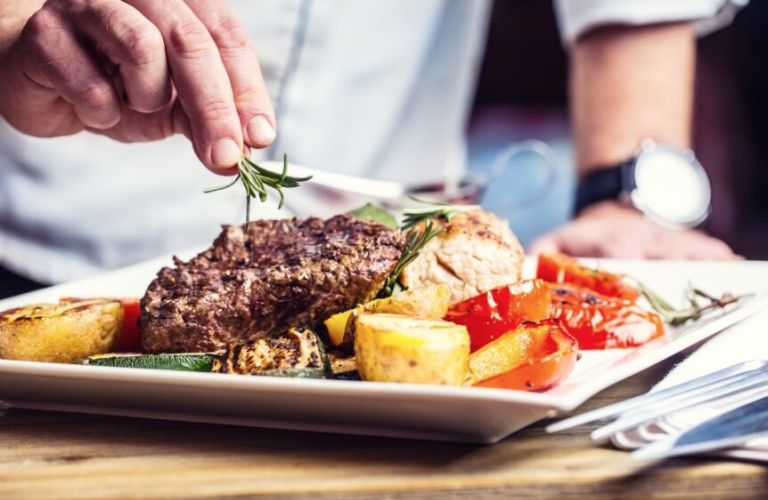 A chef garnishing a steak meal