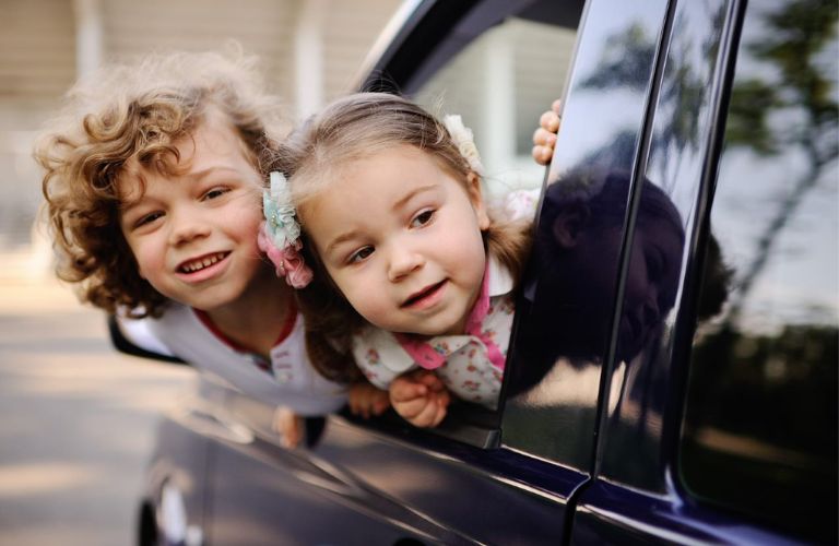 Two kids looking out of the window of a minivan.