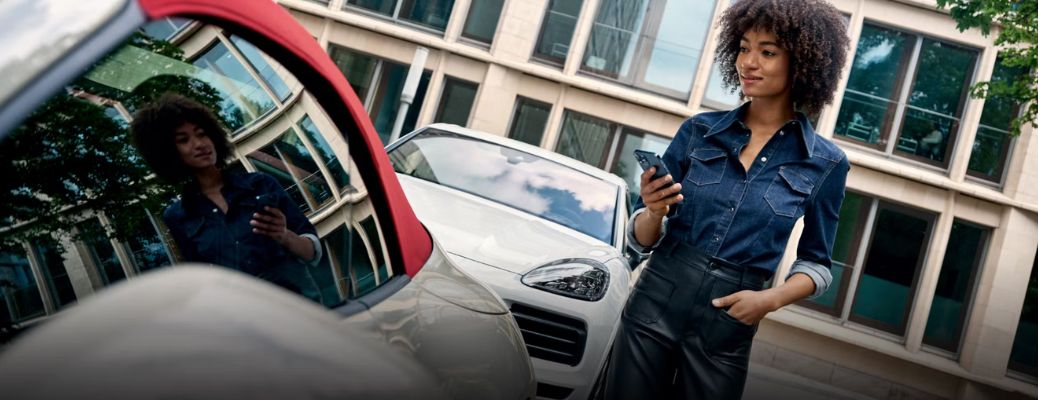 a woman on her phone next to a Porsche