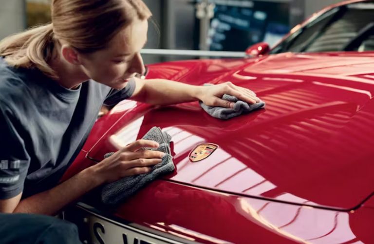 A technician cleaning the hood of a Porsche