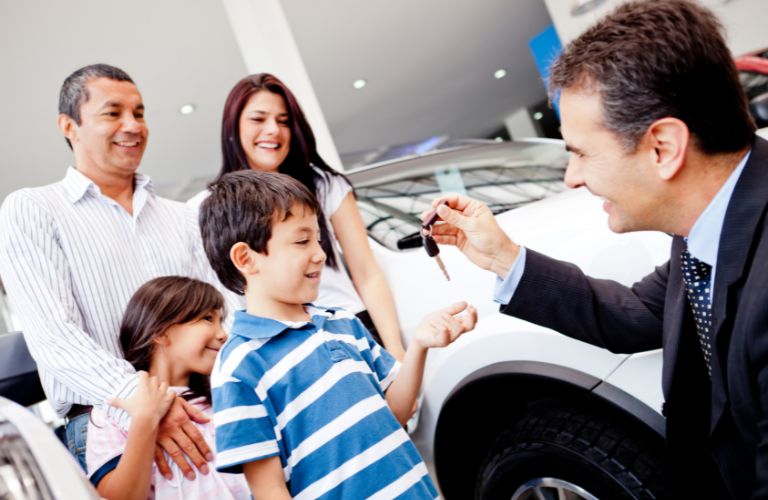 a salesman handing car keys to kids at a dealership