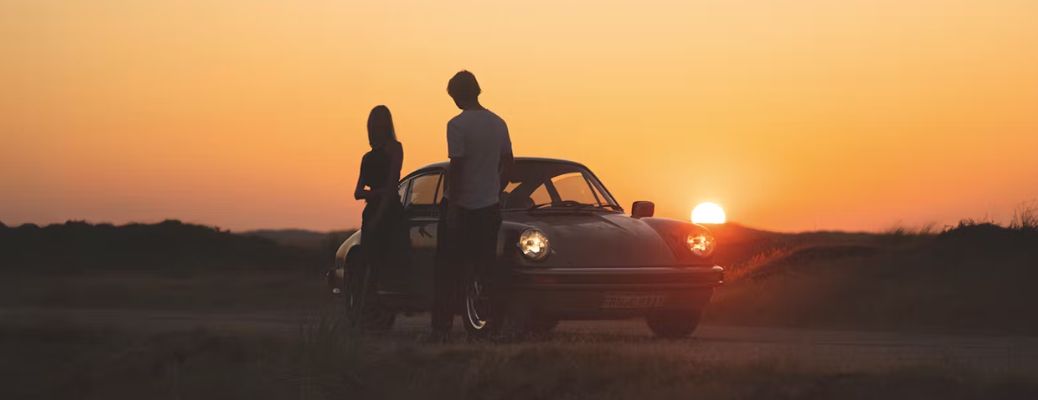 Two people posing beside a Porsche vehicle