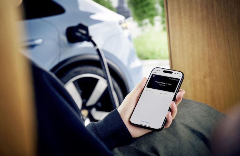 A man holding a mobile phone while his 2026 Porsche Macan Electric is charging
