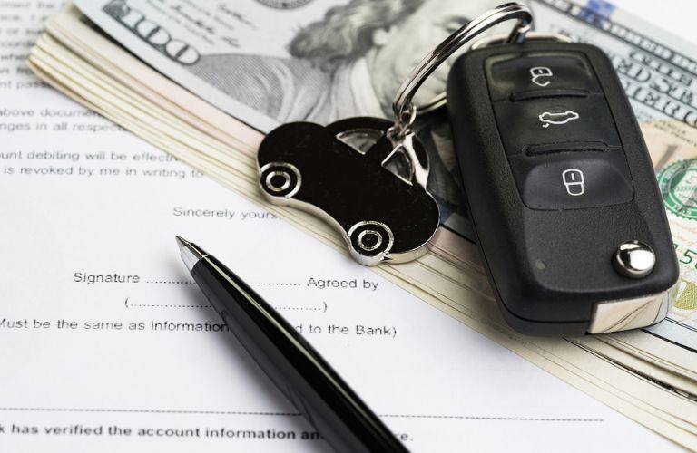 A key fob, pen, and money lying on top of a paper