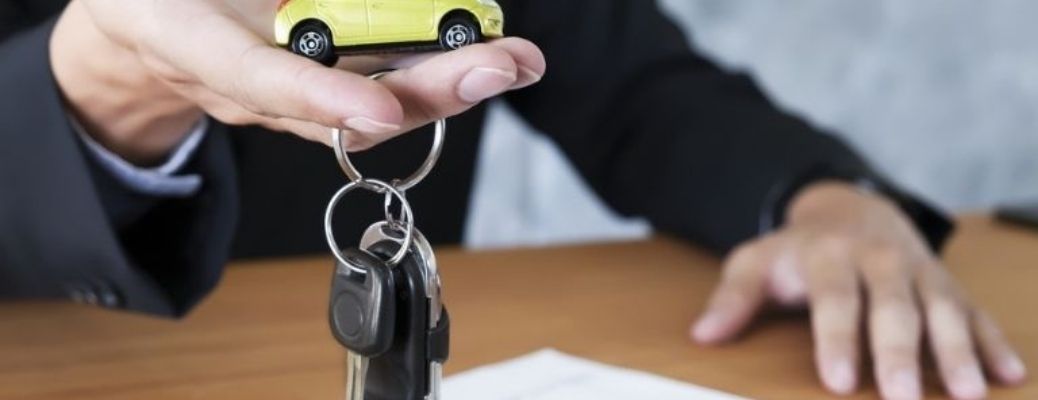 Hand of man with car keys and a miniature car