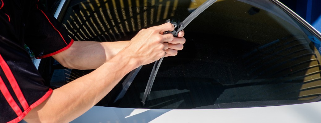 two hands holding a windshield wiper over a white car