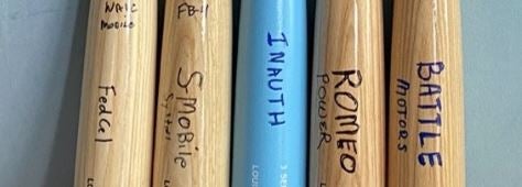 Collection of engraved baseball bats displayed on wall representing Michael Patterson's entrepreneurial ventures and companies