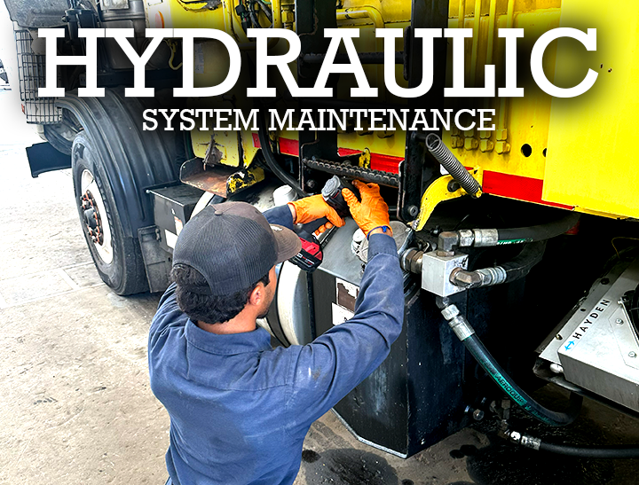 Hydraulic system maintenance on a commercial truck as a mechanic inspects hoses and fittings in a service bay.