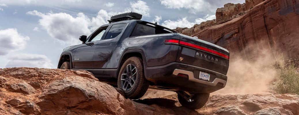 A Rivian R1T driving over rocky terrain.