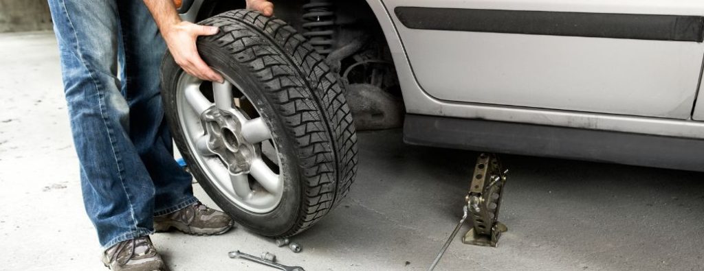 a person holding a tire and wheel by a car