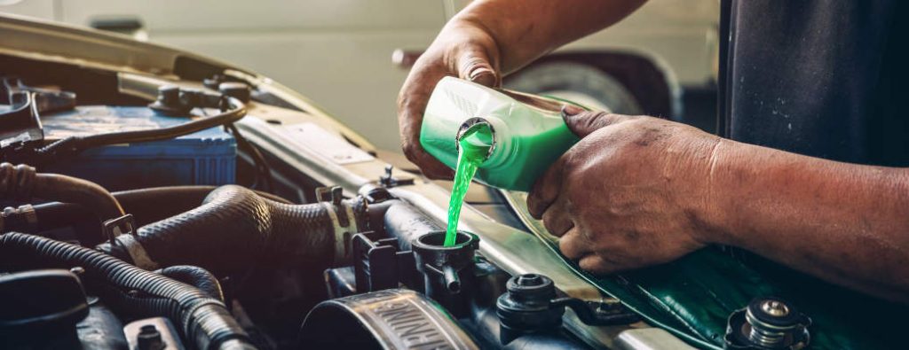 Male professional mechanic pouring antifreeze coolant liquid into car engine radiator in service center, car repair shop. Concept of car radiator coolant maintenance