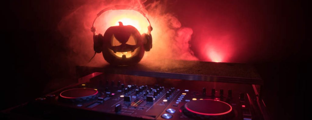 Halloween pumpkin on a dj table with headphones on dark background with copy space. Happy Halloween festival decorations and music concept. Empty space. Selective focus