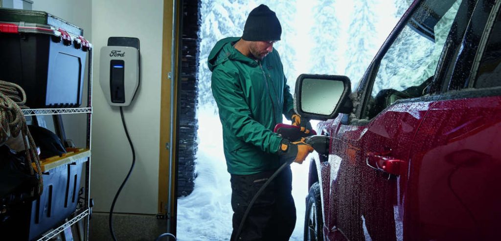 A man charging his Ford EV during a winter snowstorm. Properly charging your EV is one of the key winter EV driving tips.