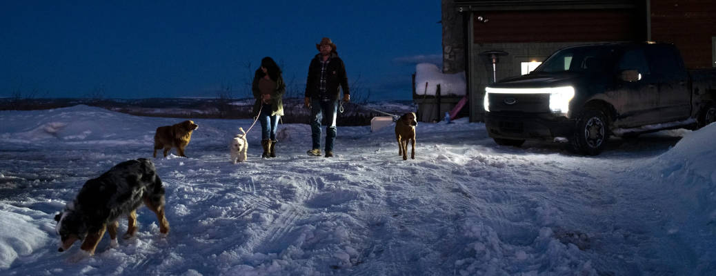 A couple walking their dogs in the snow near their Ford EV