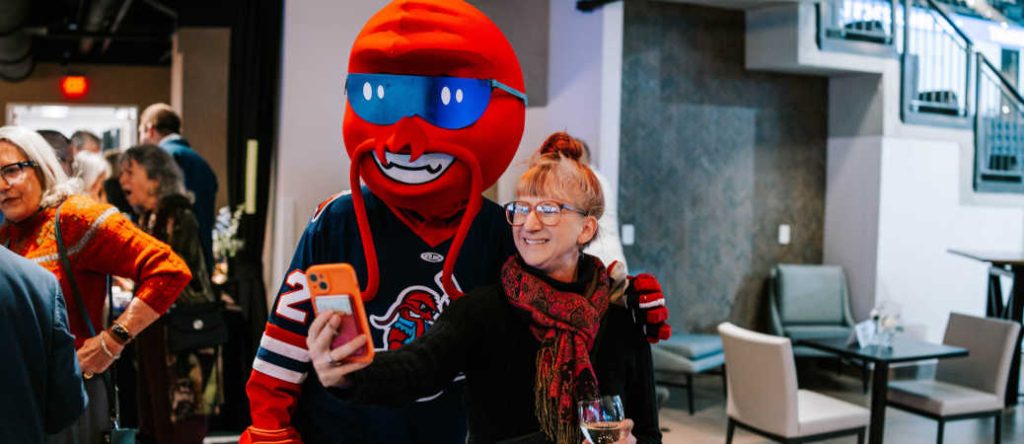A woman taking a selfie at Akins Ford Arena with the Rock Lobsters mascot