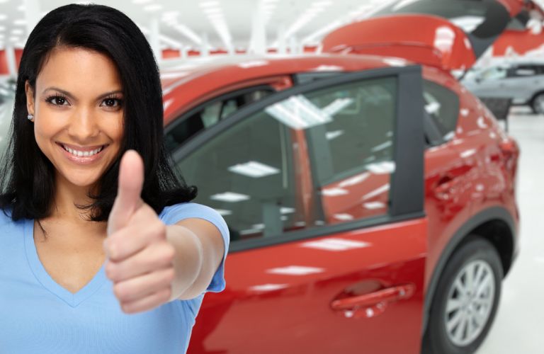 a woman smiling and showing thumbs up next to a car
