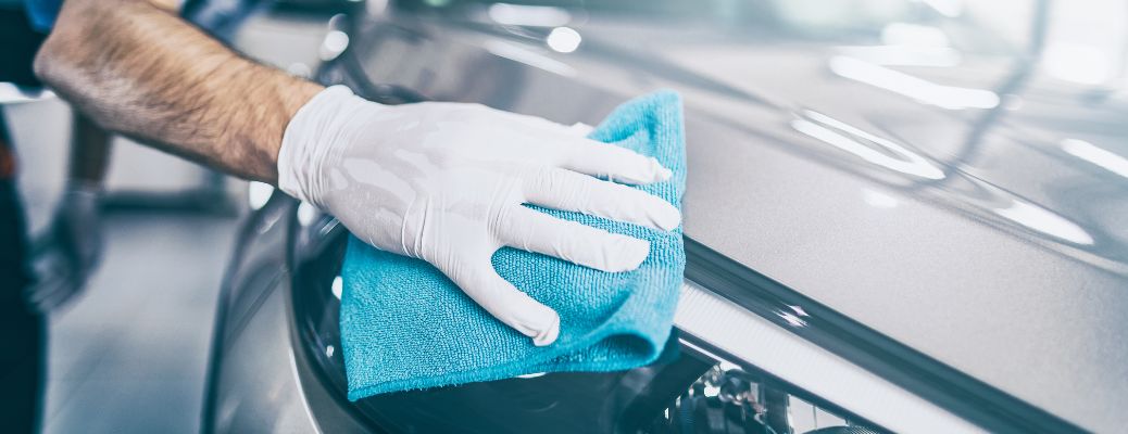 a white-gloved hand with a teal rag washing a car