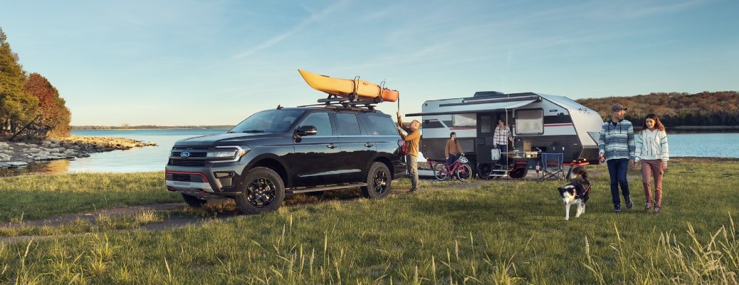 Ford Expedition SUV towing a trailer with a family nearby and water in the background