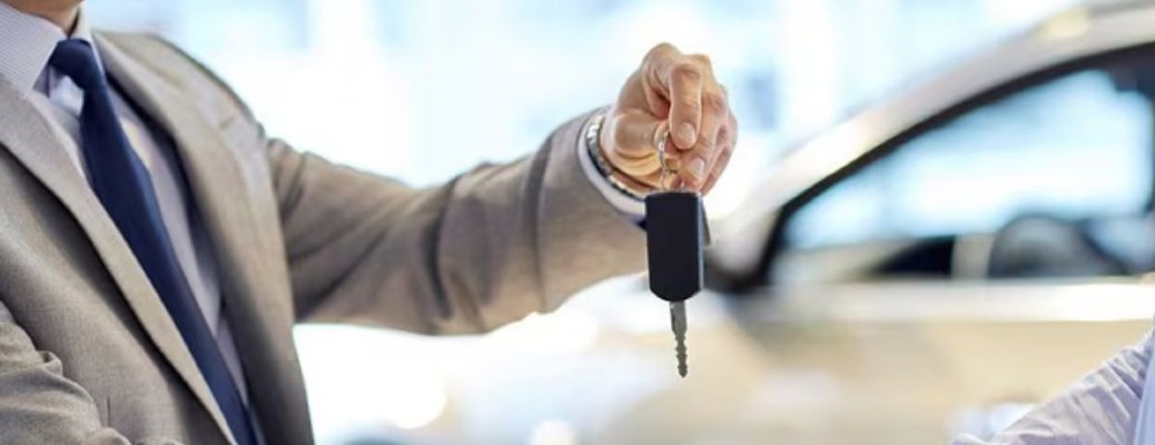 A person holding up a Ford key by a car
