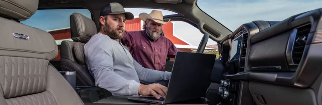 two men looking at a laptop in a truck