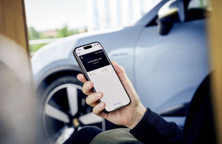 Hand of a man holding a mobile phone with a Porsche vehicle parked in the background