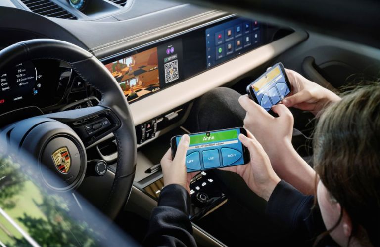 Two people holding mobile phones and playing game inside their 2026 Porsche Macan Electric