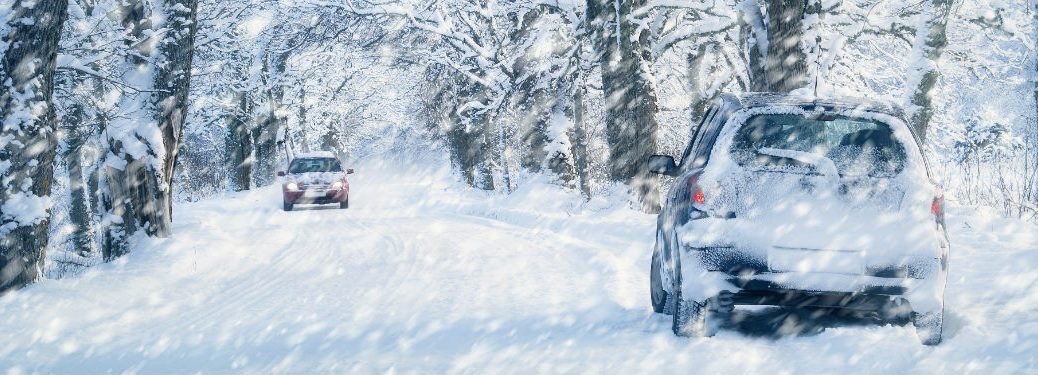 two cars driving down a very snowy, tree-lined road