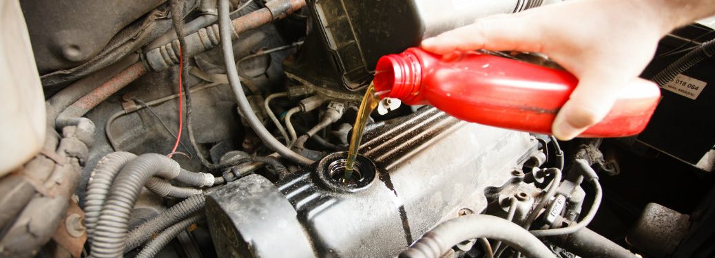 person pouring oil into an engine from a red plastic oil container