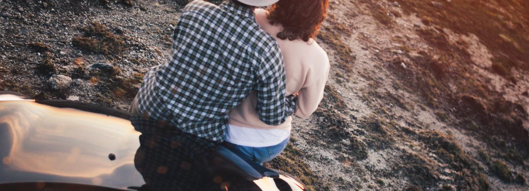 couple sitting on the hood of a car hugging