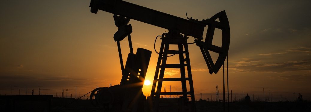 An oil pump pumps oil in a desert at sunset.